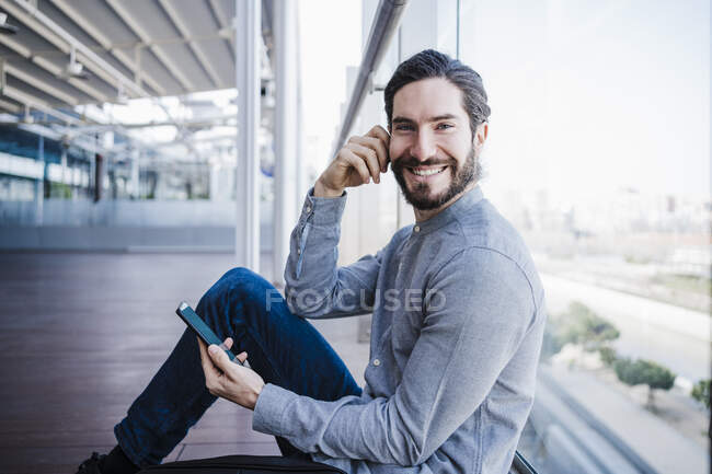 Smiling businessman with smart phone sitting at work place balcony — Stock Photo