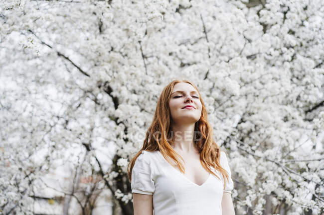 Smiling redhead woman with eyes closed in front of almond tree — Stock Photo