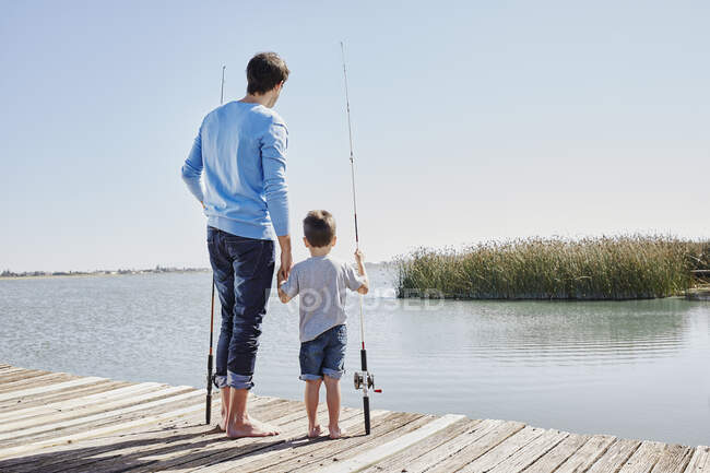 Padre e figlio che si tengono per mano mentre sono in piedi con canne da pesca sul molo — Foto stock