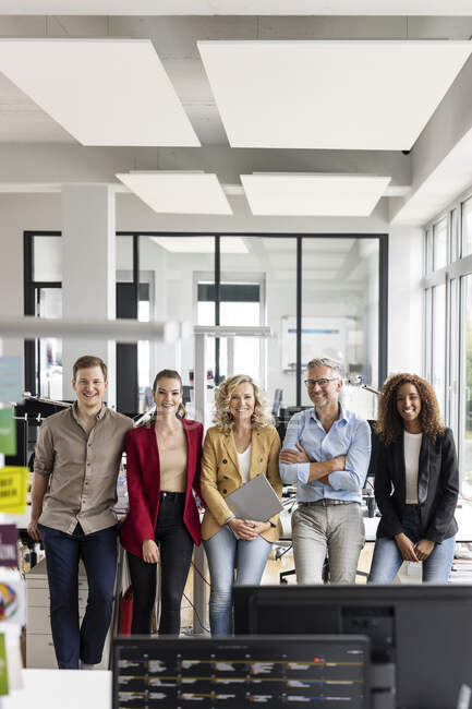 Усміхнена ділова жінка з цифровою табличкою стоїть серед чоловіків і жінок колег проти офісу — стокове фото