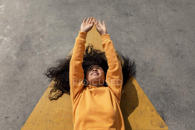 Souriant jeune femme avec les bras levés couchés sur footpat — Photo de stock