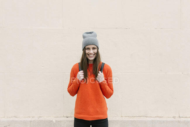 Giovane donna sorridente in maglione arancione in piedi contro il muro — Foto stock