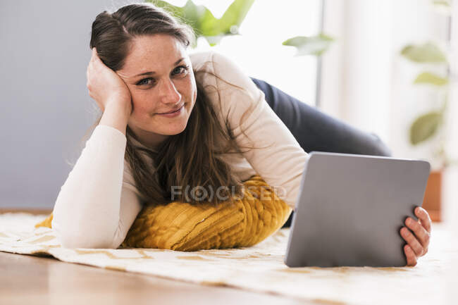 Entspannte Frau mit digitalem Tablet liegt zu Hause auf Teppich — Stockfoto