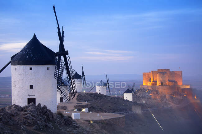 Espanha, Província de Toledo, Consuegra, Moinhos de vento históricos ao entardecer com Castelo de La Muela ao fundo — Fotografia de Stock