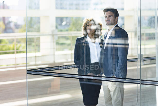 Business people looking away while standing by glass window in modern office — Stock Photo