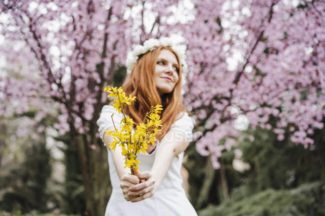 Mujer joven sosteniendo un ramo de flores amarillas de pie frente al  almendro mientras mira hacia otro lado — Veinte años, Color: - Stock Photo  | #490882778