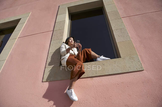 Giovane donna con smart phone seduto sul davanzale della finestra di costruzione — Foto stock
