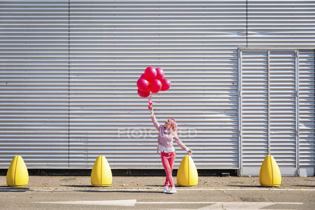 Frau in pinkfarbener Jacke betrachtet Luftballons auf der Straße — Stockfoto