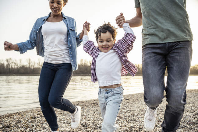 Verspielte Familie hält Händchen beim Laufen am See — Stockfoto