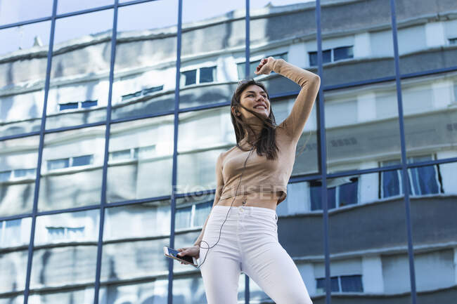 Woman with mobile phone dancing against modern glass building — Stock Photo
