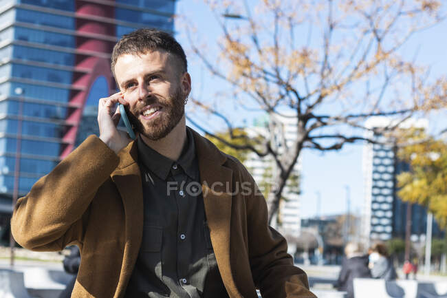 Взрослый бизнесмен улыбается, разговаривая по мобильному телефону, стоящему в городе — стоковое фото