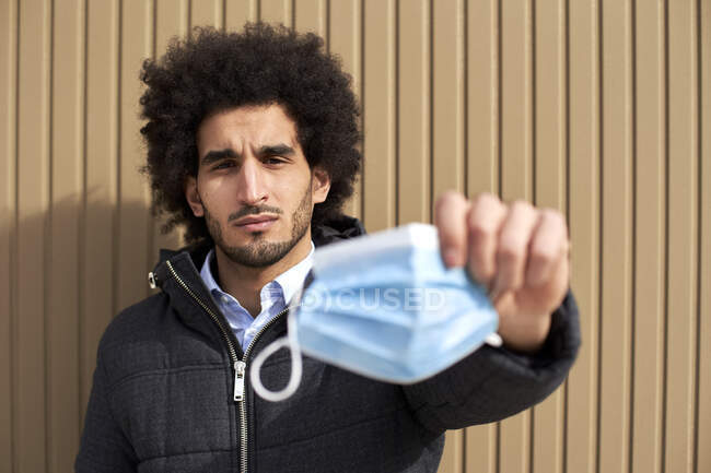 Afro man holding protective face mask by wall during COVID-19 — Stock Photo