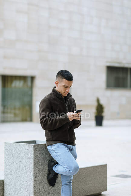 Jeune homme utilisant un téléphone intelligent tout en se tenant contre la construction — Photo de stock