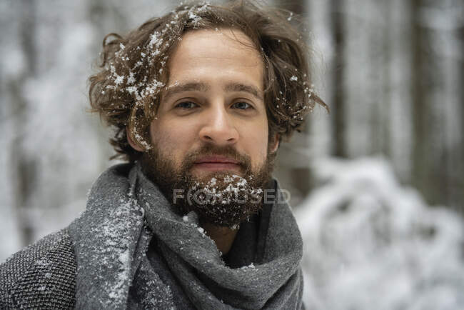 Молодий чоловік з волоссям і бородою вкритий снігом дивиться, стоячи в лісі — стокове фото
