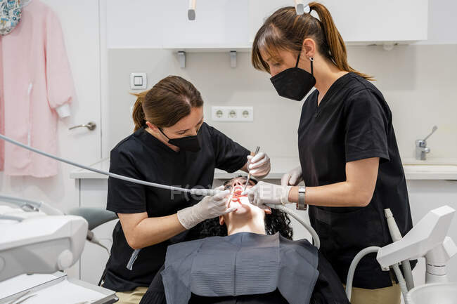 Dentistas limpiando dientes de paciente en clínica médica - foto de stock