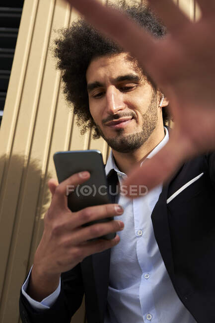 Hombre adulto medio usando el teléfono inteligente por la pared durante el día soleado - foto de stock