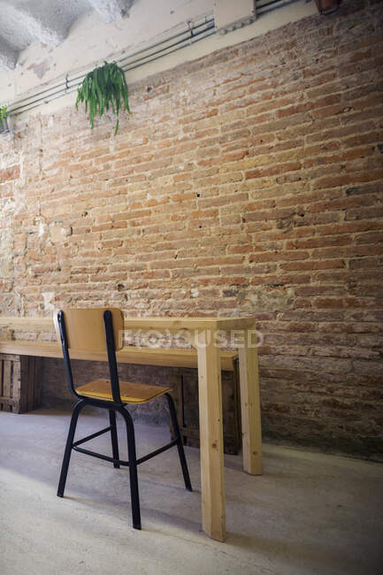 Стілець і порожній стіл стоять перед цегляною стіною. — стокове фото