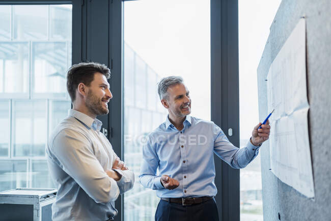 Profissionais do sexo masculino discutindo sobre papel no quadro de avisos no local de trabalho — Fotografia de Stock