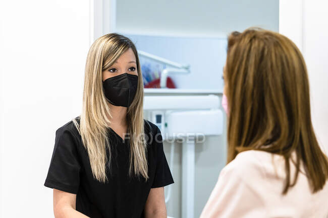 Junge Zahnärztin mit Schutzmaske diskutiert mit Kollegin in Klinik während COVID-19 — Stockfoto