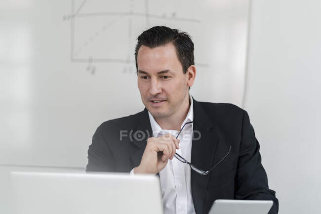 Homme d'affaires tenant des lunettes tout en regardant ordinateur portable au bureau — Photo de stock
