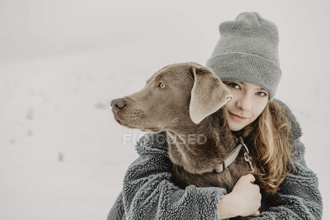 Портрет дівчини - підлітка, що сидить у снігу і обіймає Лабрадор Ревевер. — стокове фото