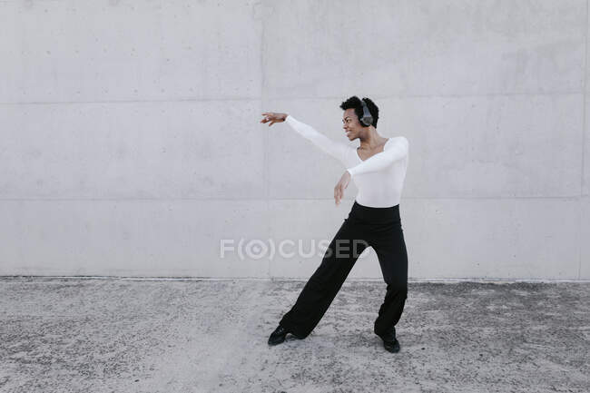 Uomo flessibile con le cuffie che ballano contro il muro bianco — Foto stock