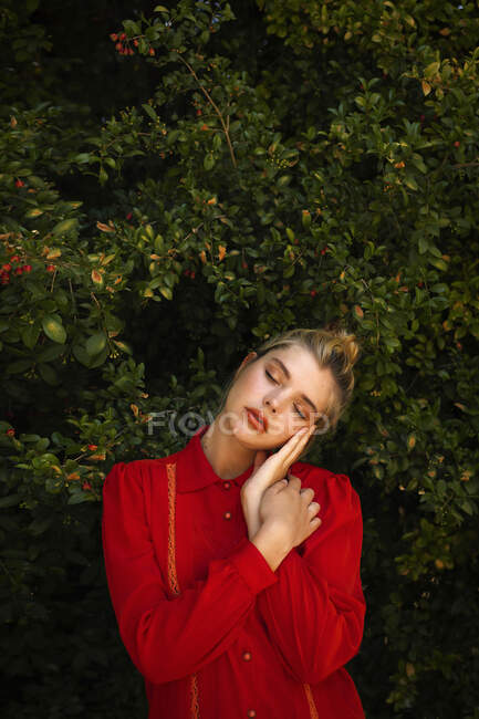 Giovane donna bionda in camicia rossa in piedi contro le piante — Foto stock
