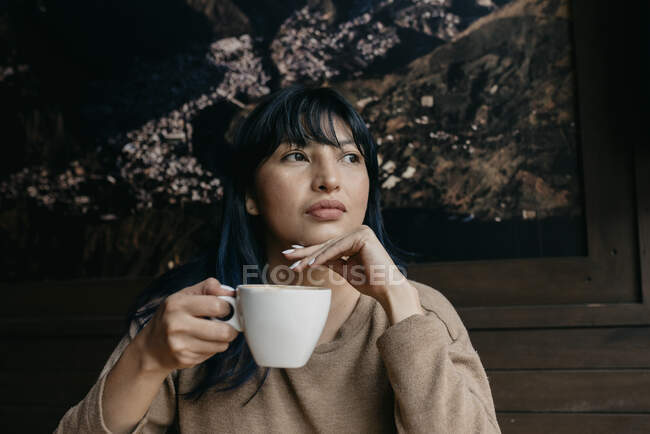 Женщина с рукой на подбородке, держа кофе, отворачиваясь — стоковое фото