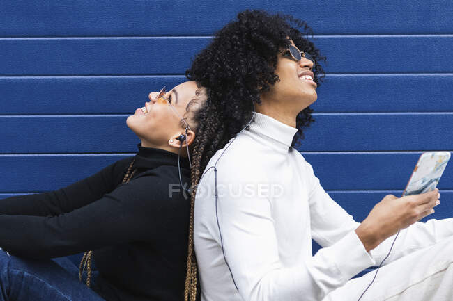 Couple wearing sunglasses looking up while sitting against blue wall — Stock Photo