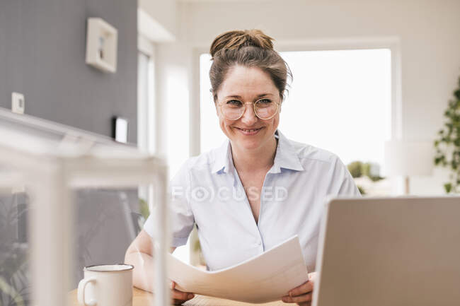 Donna d'affari sorridente con documento seduto alla scrivania — Foto stock