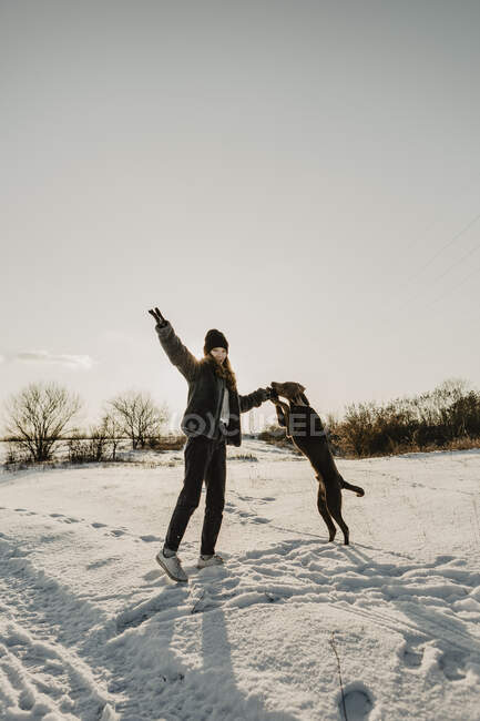 Teenagermädchen spielt im Morgengrauen mit Hund im Schnee — Stockfoto
