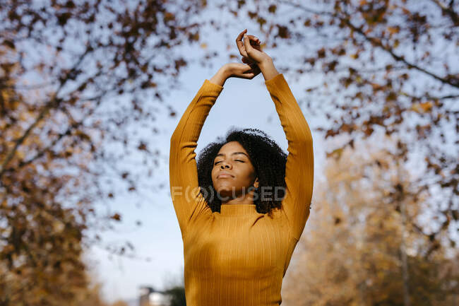 Afro woman with hands raised in park during sunny day — Stock Photo
