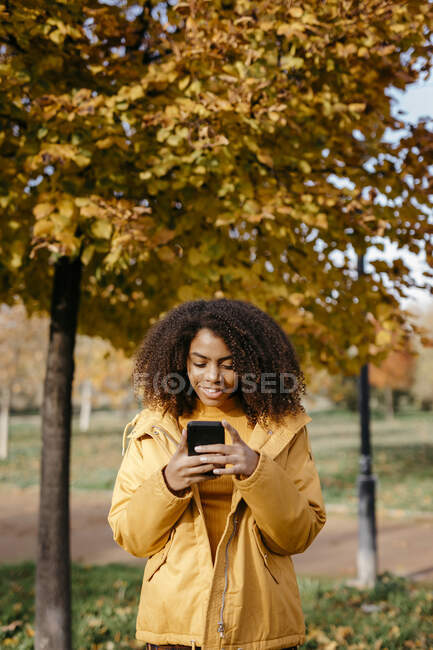 Junge Afrofrau im Herbst im Park mit Smartphone — Stockfoto