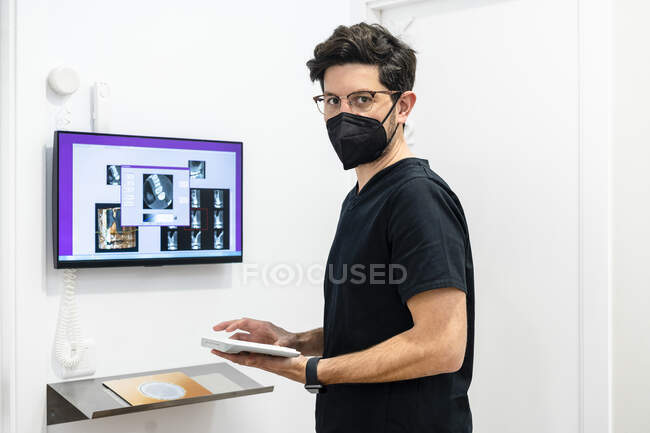 Dentiste masculin portant un masque protecteur tenant le clavier de l'ordinateur à la clinique — Photo de stock