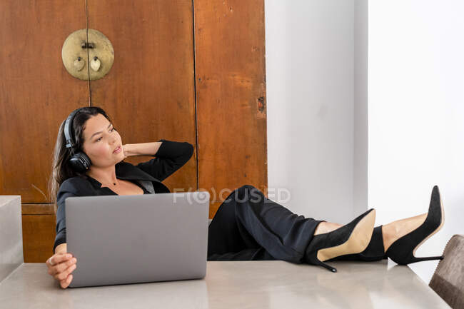 Female entrepreneur wearing headphones sitting with laptop by table at home — Stock Photo