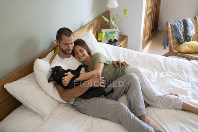 Verspieltes Paar umarmt Mops Dog, während er zu Hause im Bett liegt — Stockfoto