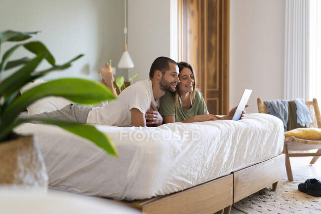 Casal jovem usando laptop enquanto deitado na cama no quarto em casa — Fotografia de Stock