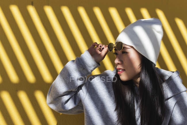 Woman removing sunglasses against yellow wall — Stock Photo