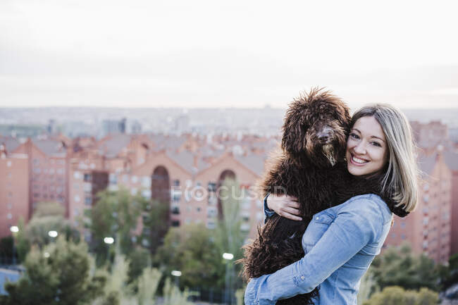 Felice bella donna che trasporta cane da paesaggio urbano — Foto stock