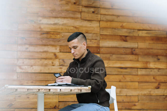 Молодий чоловік - підприємець користується смарт - телефоном, сидячи у тротуарі. — стокове фото