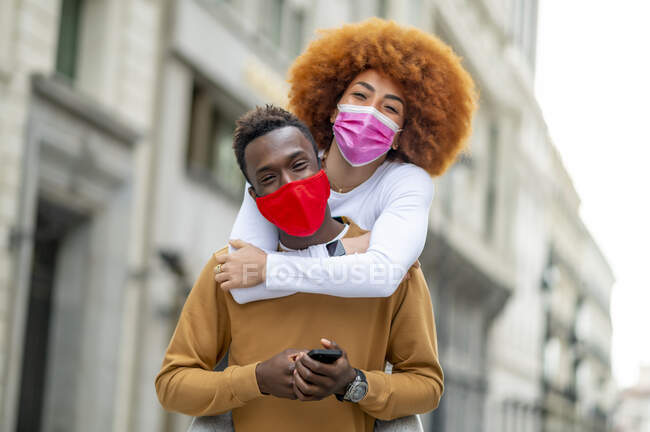 Woman wearing face mask piggybacking on man in city — Stock Photo