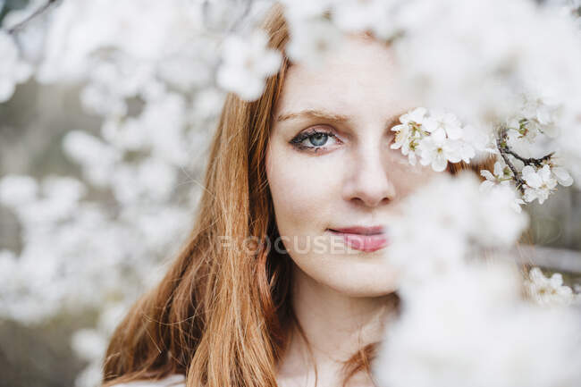 Schöne junge Frau mit grauen Augen inmitten eines weißen Mandelbaums — Stockfoto