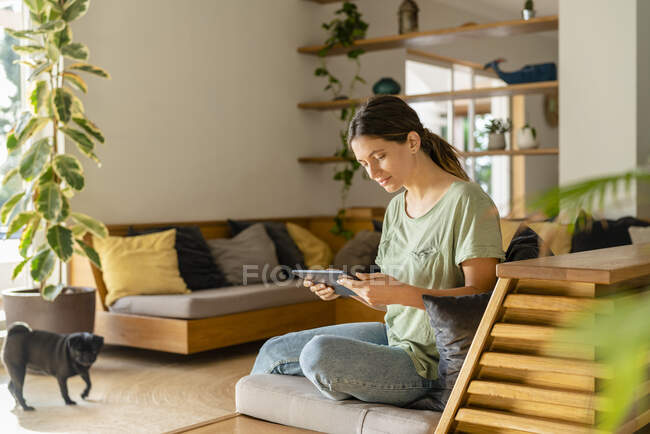 Молодая женщина с помощью цифрового планшета, сидя дома на диване — стоковое фото