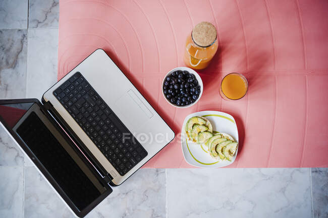 Ordinateur portable et petit déjeuner sain sur tapis d'exercice à la maison — Photo de stock