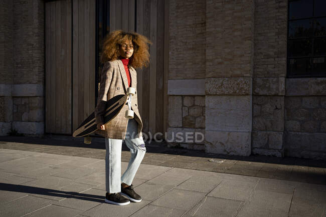 Afro mujer llevando monopatín mientras camina por sendero — Stock Photo