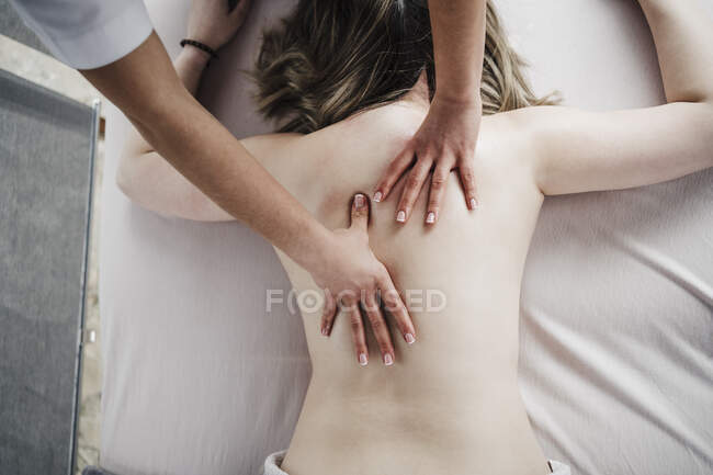 Fisioterapeuta femenina masajeando la espalda de una paciente sin camisa acostada en frente en el hospital - foto de stock