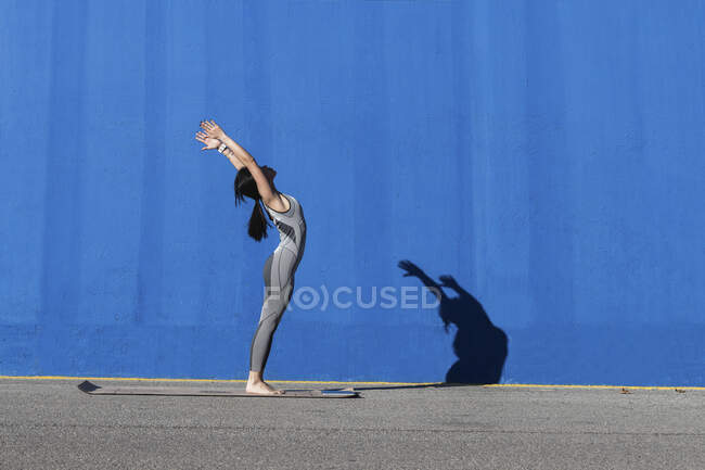 Жінка робить вправи на килимку біля блакитної стіни. — стокове фото