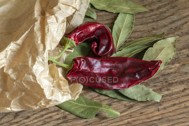 Red chili pepper and bay leaves with brown paper bag on wooden cutting board — Stock Photo