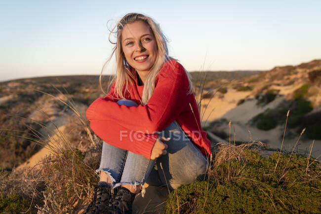 Jovem mulher abraçando joelhos enquanto sentado na duna de areia — Fotografia de Stock