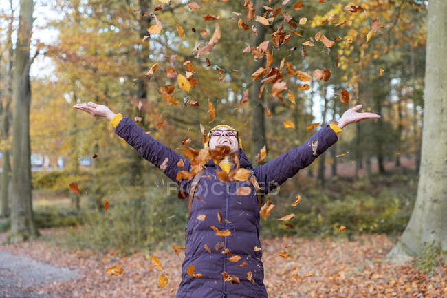 Весела жінка грає з осіннім листям у лісі — стокове фото